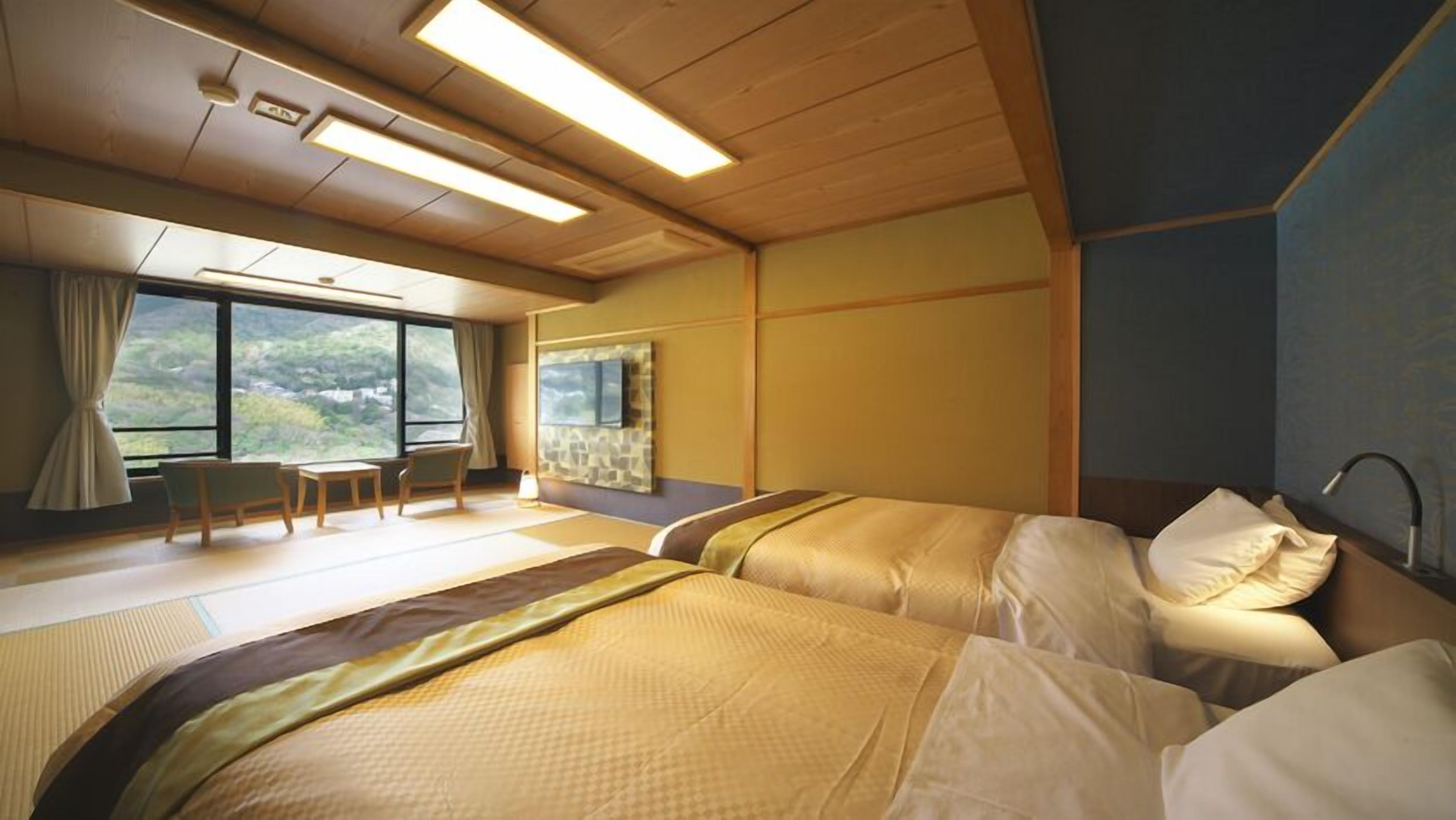 A hotel room with two beds, a small table, chairs, a window with a view, and a bathroom.