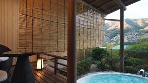 A wooden deck with a hot tub, bamboo blinds, and a view of a valley. - Hotel Zuiyo (Atami)