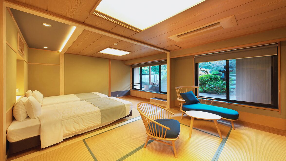 A room with a bed, a chair, a small table, and large windows.