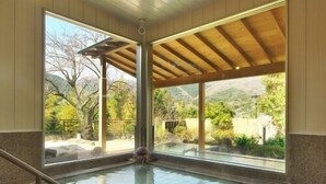 A swimming pool with a tiled floor, a wooden ceiling, and large windows offering a view of trees and hills. - Hotel Zuiyo (Atami)