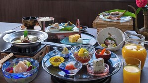 A table with various dishes and drinks, a window with a view of a cityscape, and a vase with a flower. - Hotel Zuiyo (Atami)