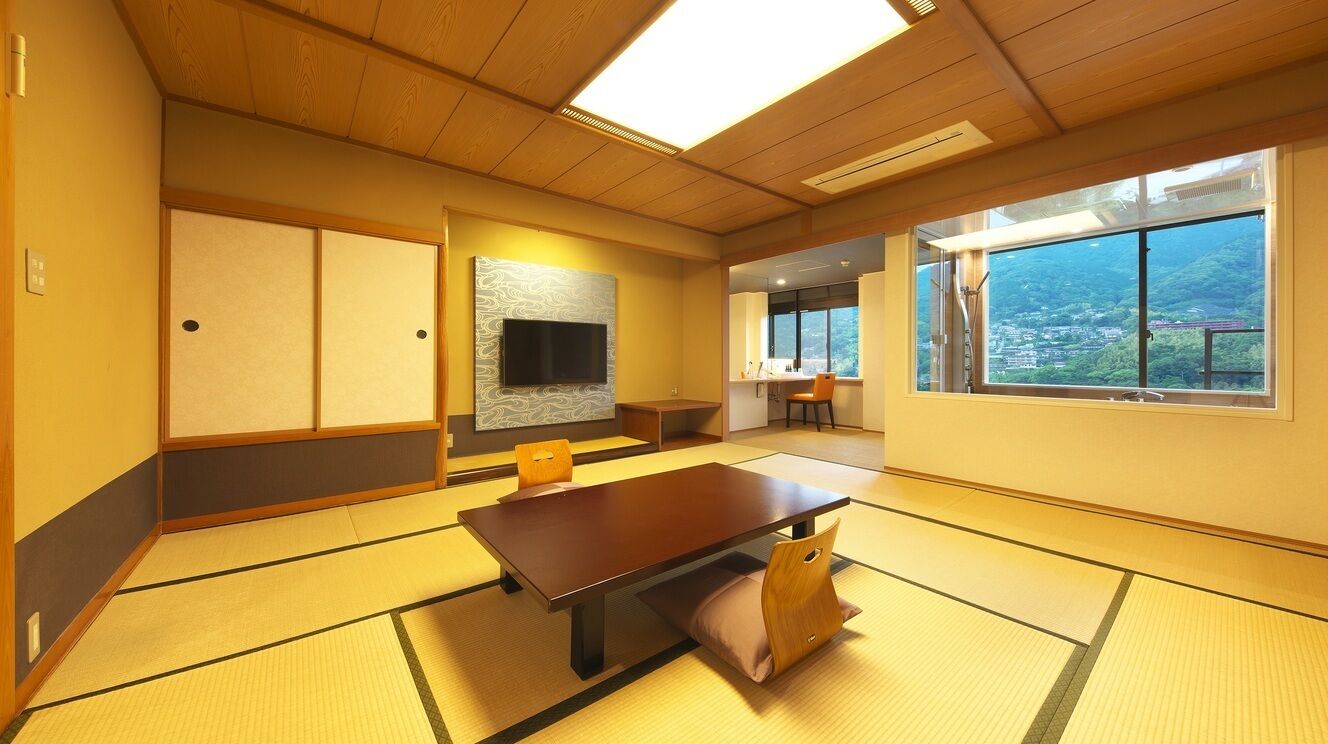 A traditional tatami room with a tatami mat floor, a low table, a television, and a sliding door.