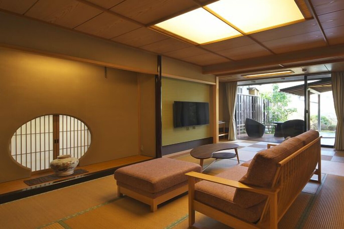 Ein traditioneller japanischer Raum mit Tatami-Boden, einem niedrigen Tisch, einer Couch und einem Fernseher.