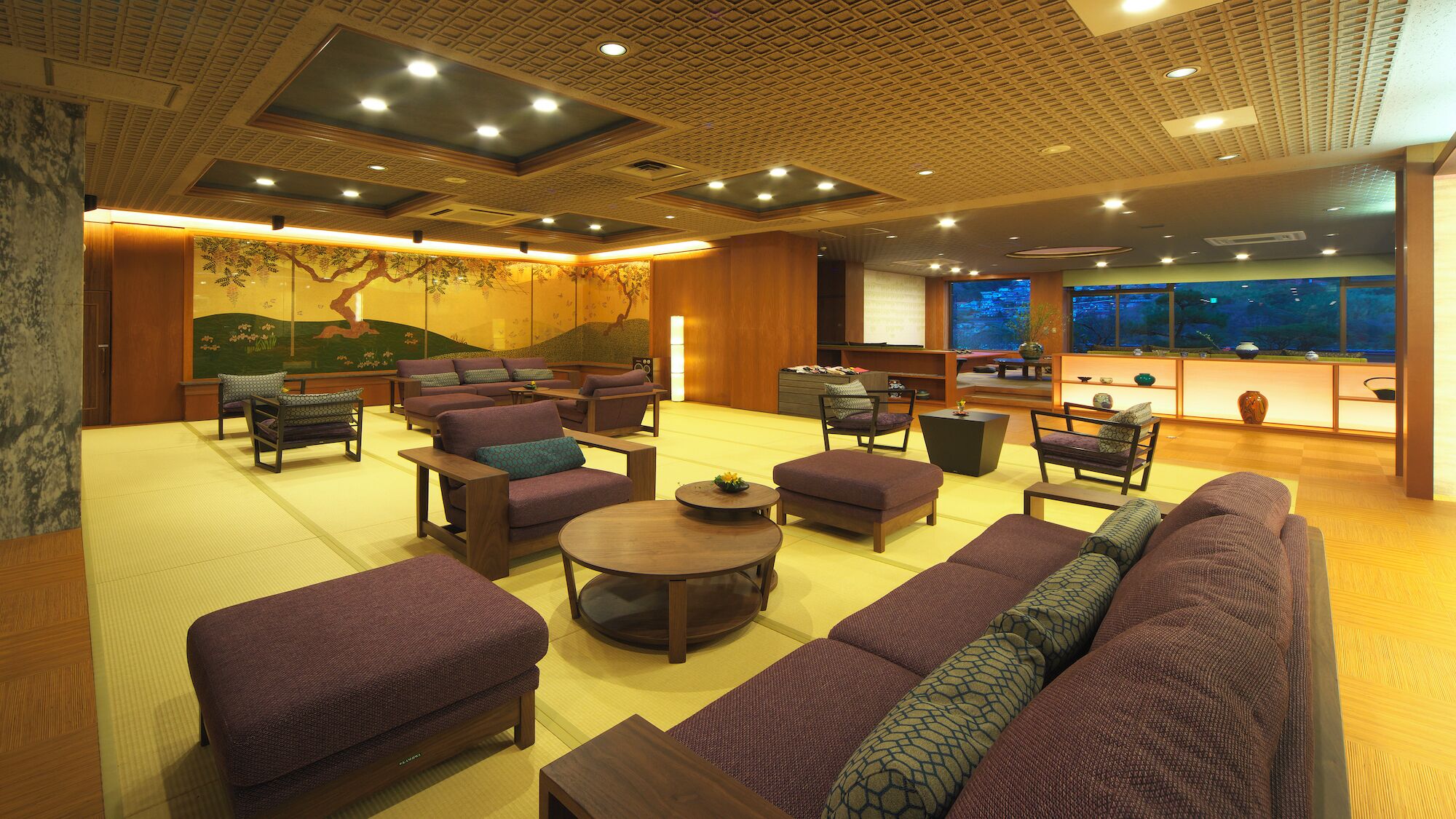 A spacious lounge area with multiple seating options, a large window offering a view, and a traditional mural on the wall.
