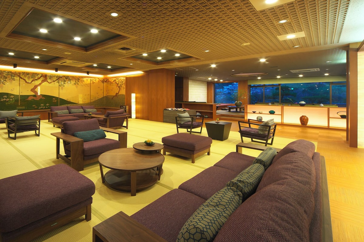 A spacious lounge area with multiple seating options, a large window offering a view, and a traditional mural on the wall.