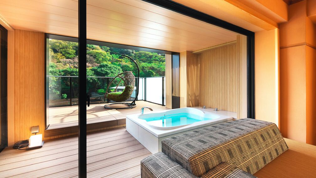 A modern bathroom with a bathtub, wooden flooring, and a view of greenery outside.