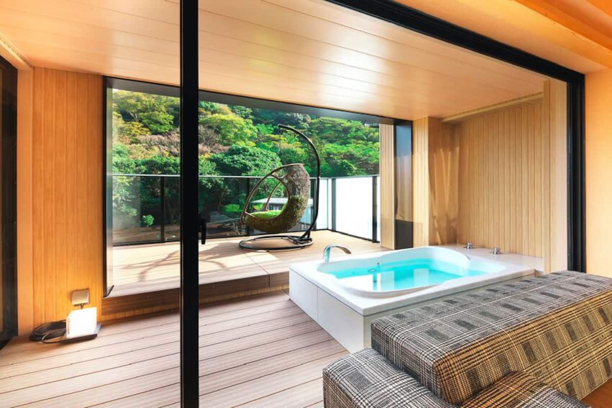 A modern bathroom with a bathtub, wooden flooring, and a view of greenery outside.