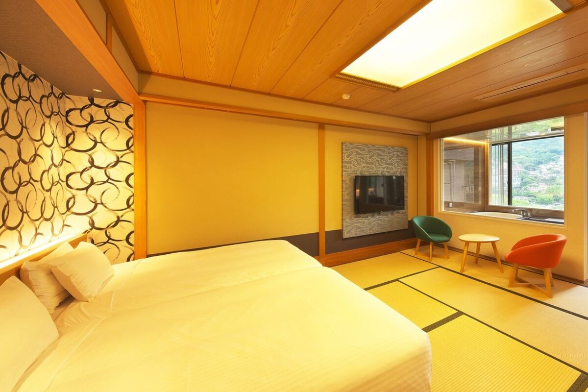 A hotel room with a bed, a television, a window, and a view of the outdoors.