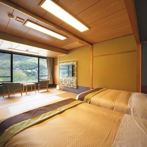 Habitación de hotel con dos camas, televisión, ventana con vista a zonas verdes y un área de descanso con sillas.
