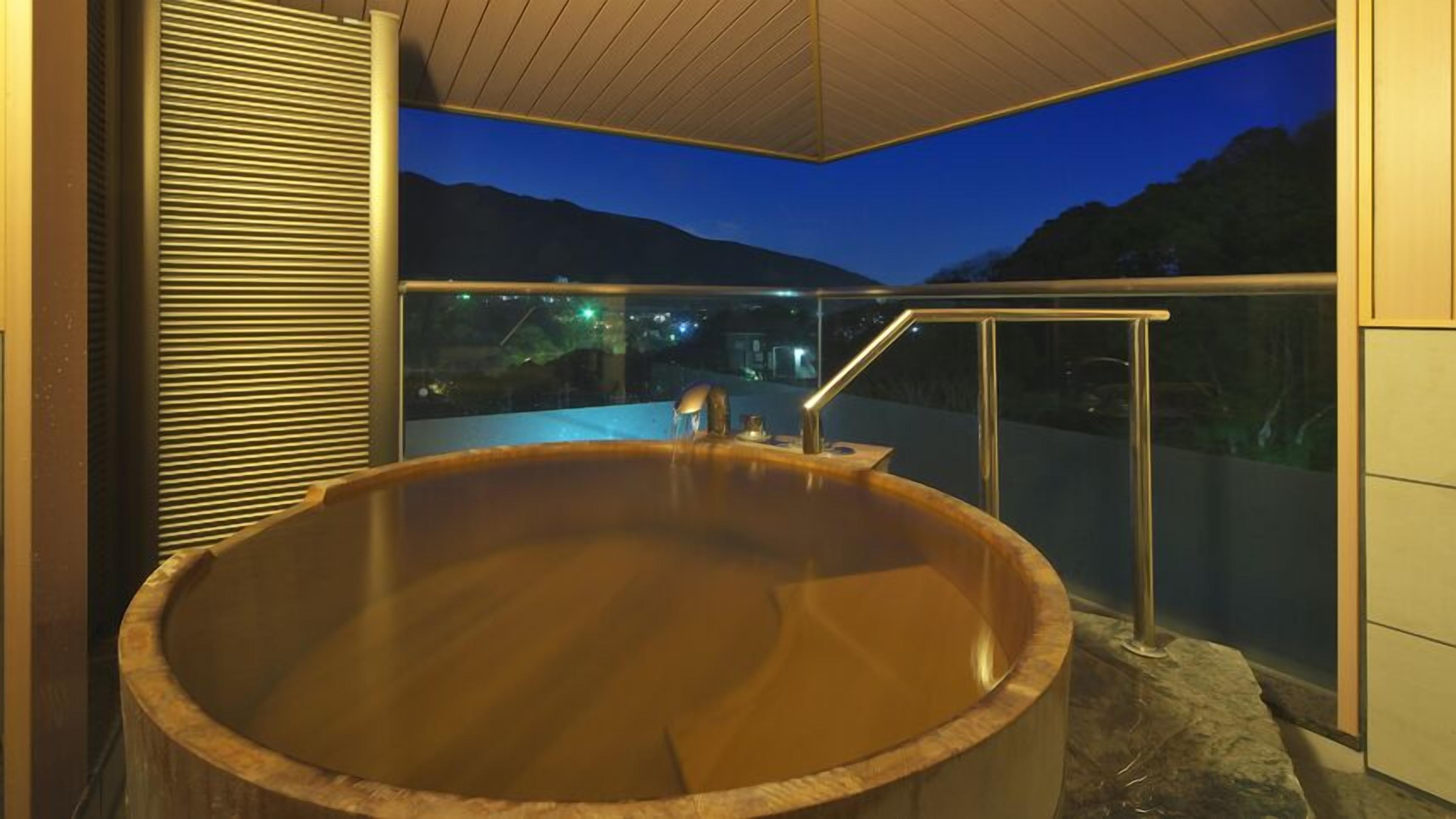 A hot tub with a wooden exterior, a metal railing, and a view of mountains at dusk.