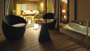 A room with a wooden floor, two black chairs, a small table, a sofa, and a bathtub. - Hotel Zuiyo (Atami)