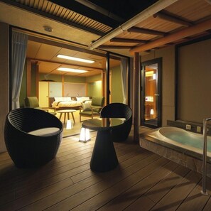A room with a wooden floor, two black chairs, a small table, a sofa, and a bathtub. - Hotel Zuiyo (Atami)