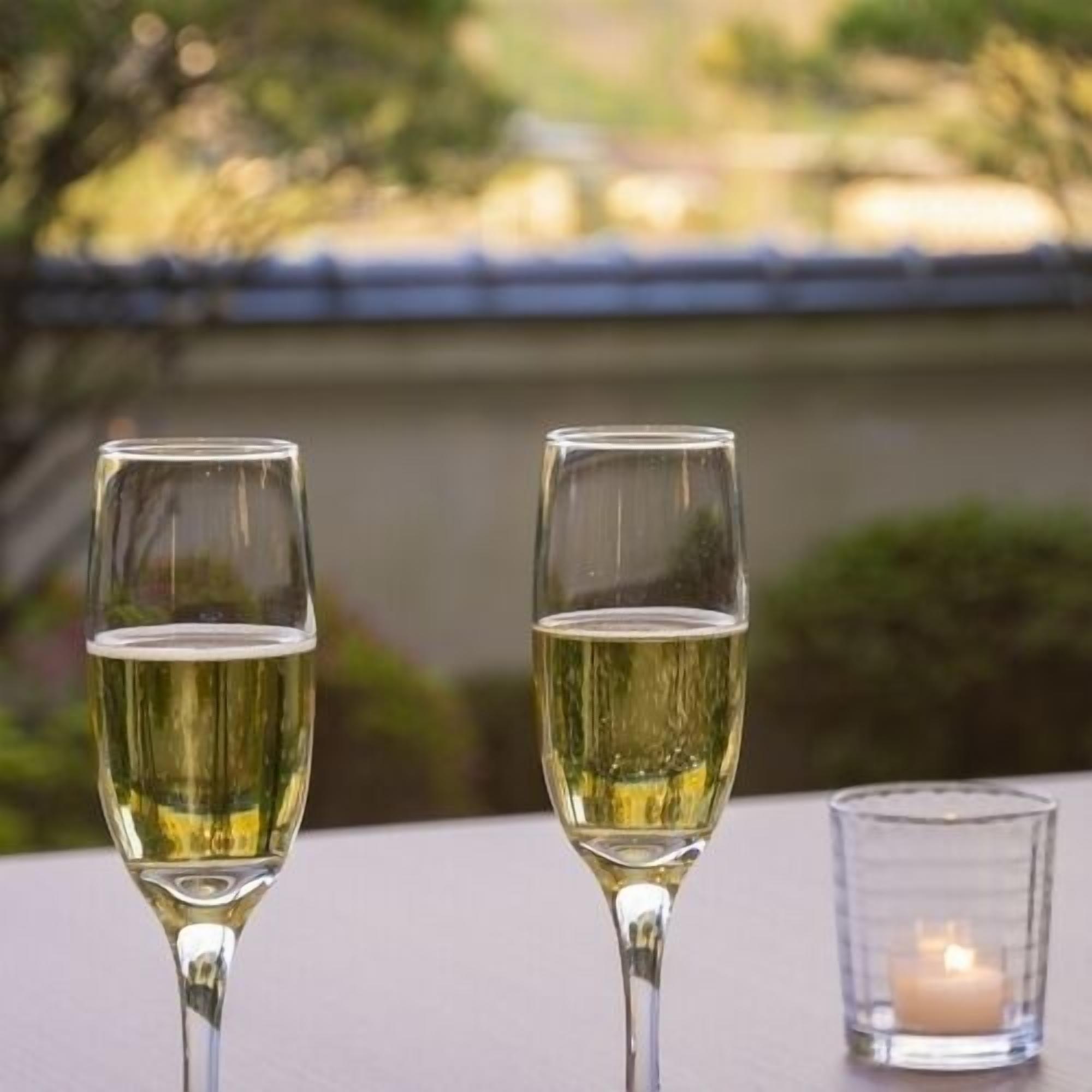 Two glasses of white wine on a table with a candle in a glass holder.