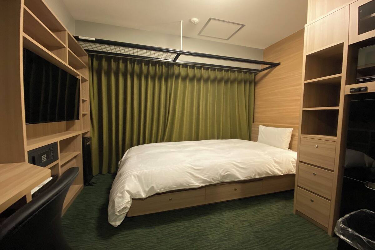 A compact hotel room with a single bed, built-in wardrobe, and a small desk area.