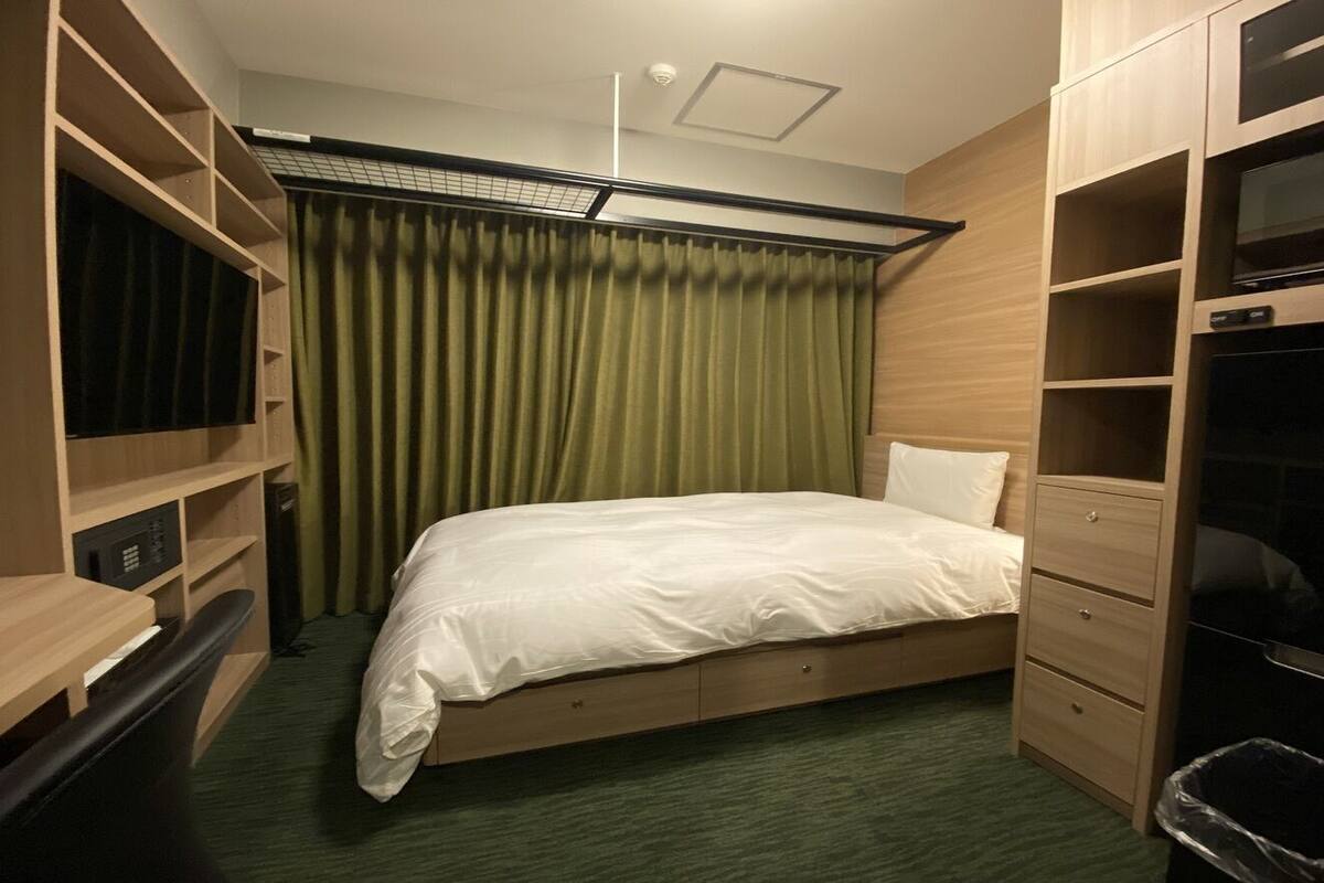 A bedroom with a bed, a desk, a wardrobe, and a trash bin.