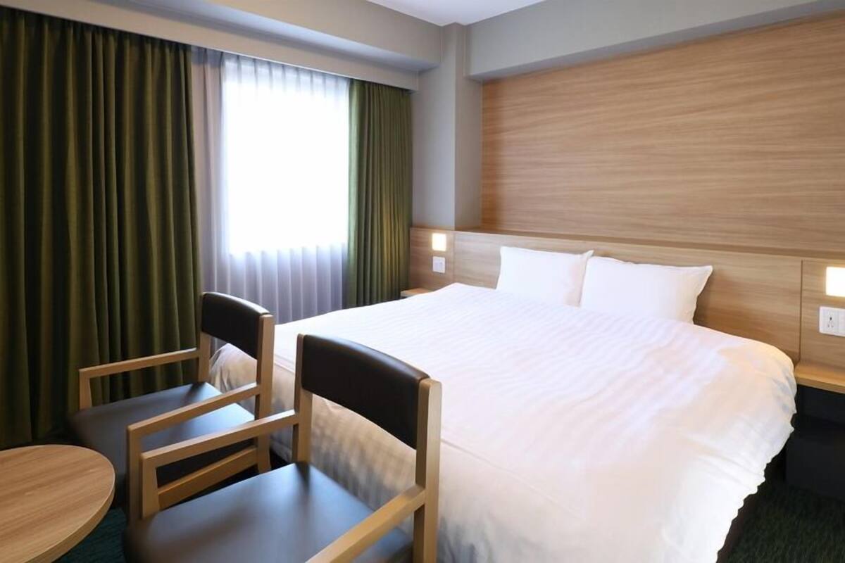 A hotel room with a bed, two chairs, a small table, and a window with curtains.