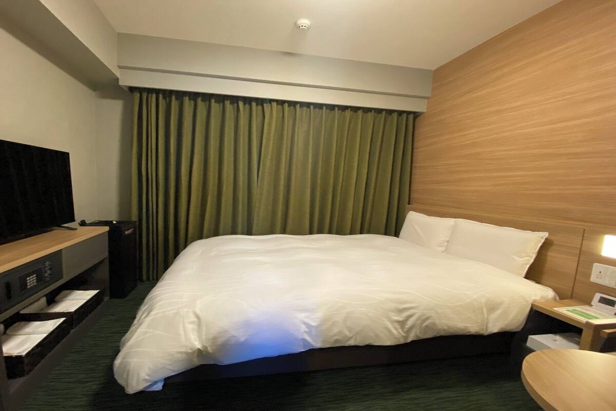 A hotel room with a bed, a desk with a computer, a television, and a curtain.