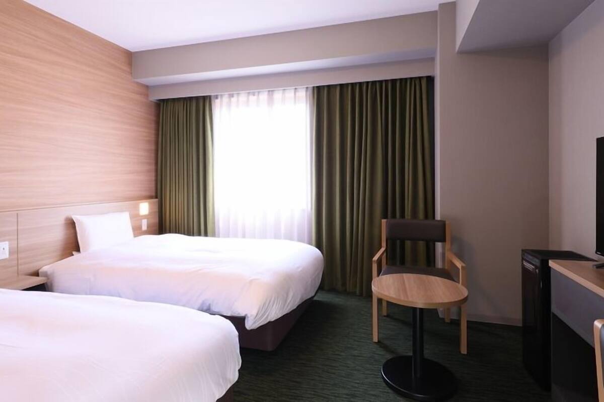A hotel room with two beds, a desk with a television, and a chair.