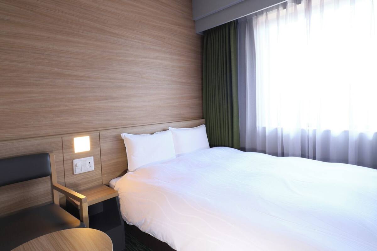A hotel room with a wooden headboard, a bedside table, a chair, and a large bed.