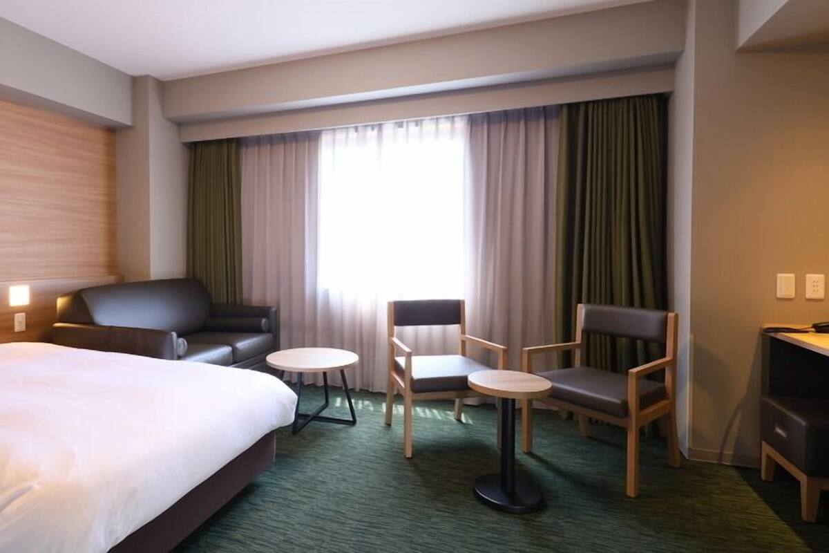 A hotel room with a bed, two armchairs, a small table, and a desk.