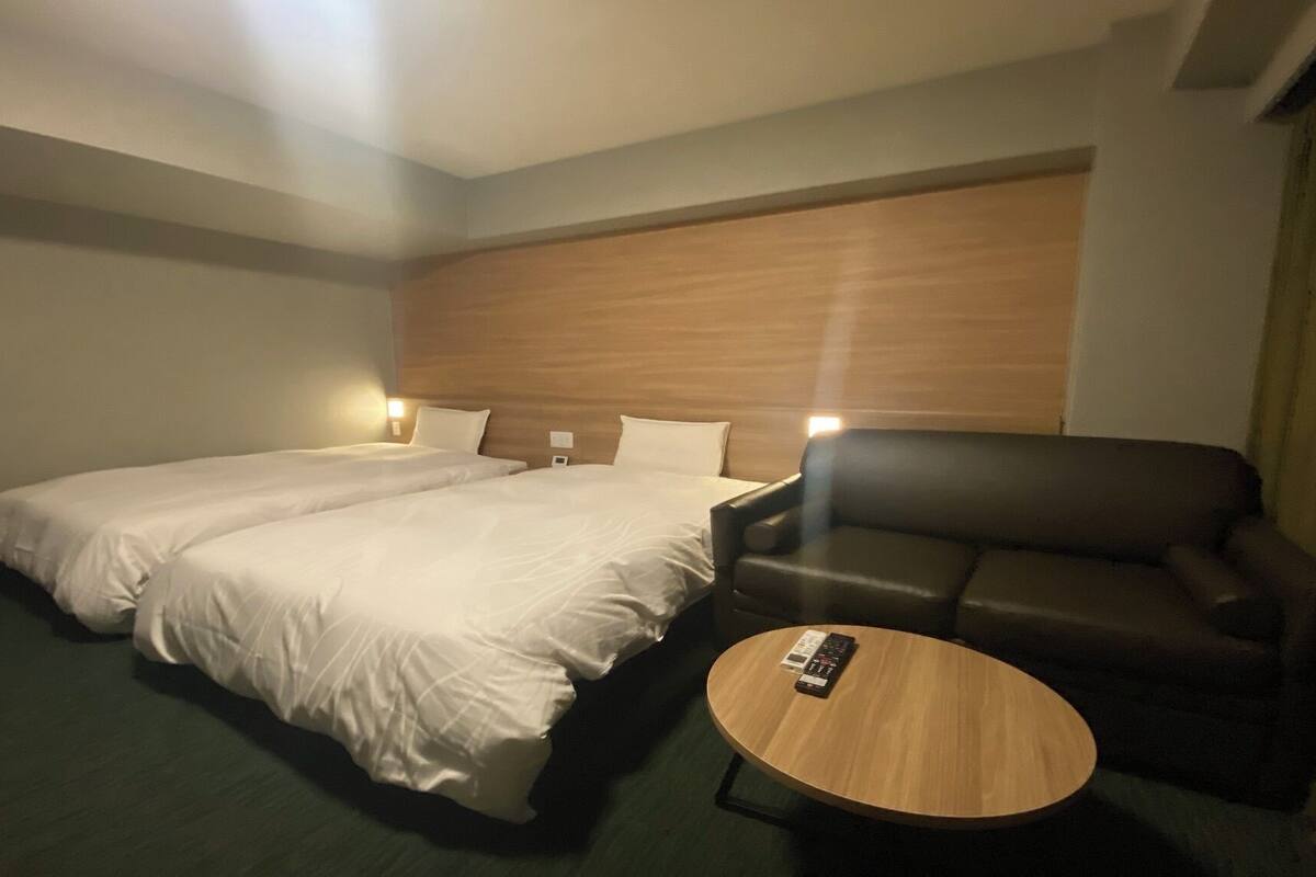 A hotel room with two beds, a leather sofa, a small wooden table, and a remote control on the table.