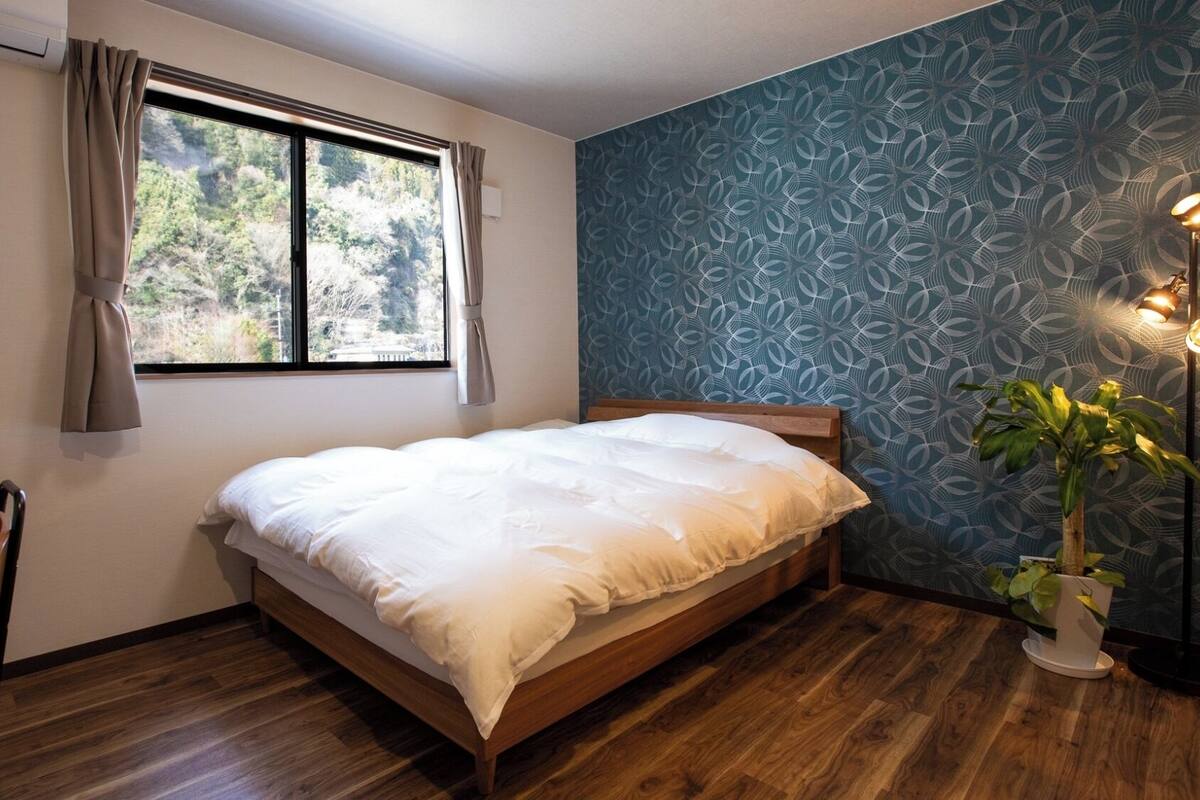 A bedroom with a bed, a window, a plant, and a lamp.