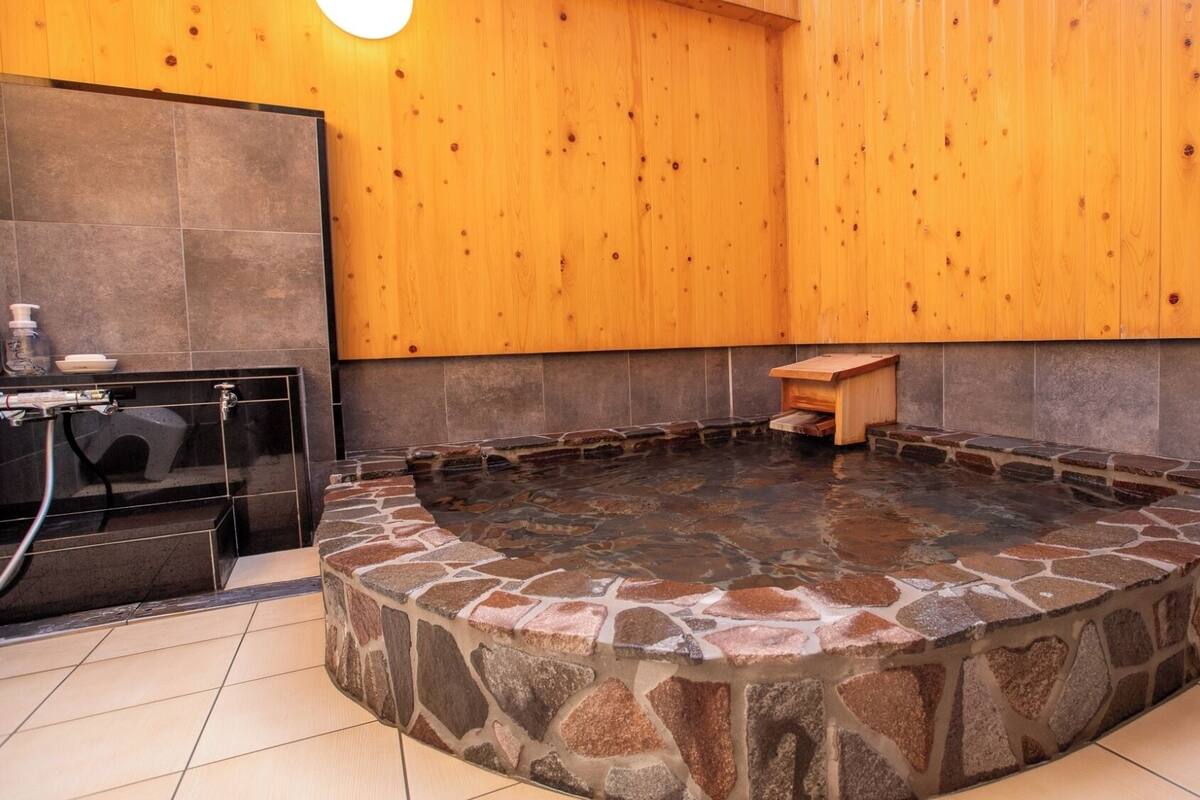 A stone hot tub with a wooden bench, a tiled floor, and wooden walls.