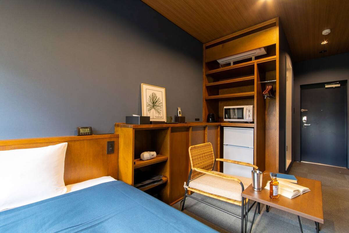Habitación de hotel con cama, una silla, una mesita con una botella, microondas y armario.