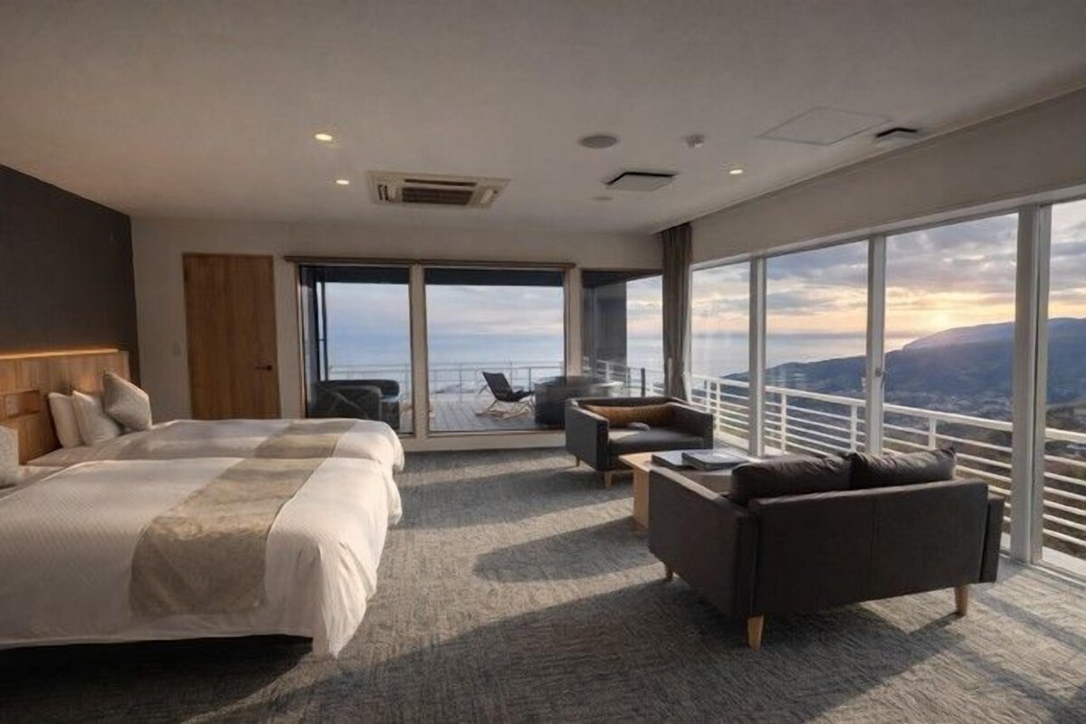 A modern hotel room with a large bed, a sofa, and a balcony with a city view.