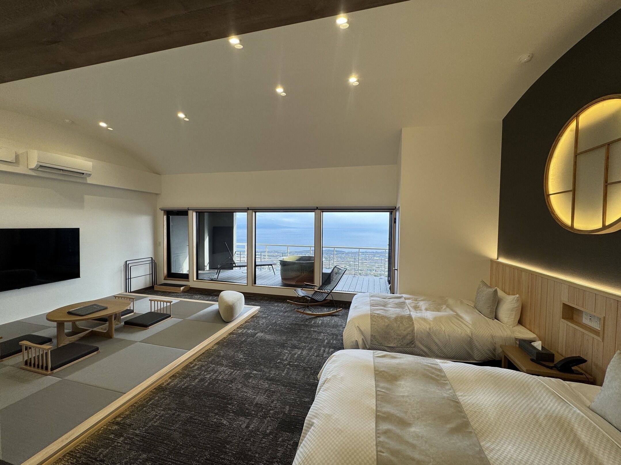 A modern hotel room with a large bed, a sofa, a dining table, and a TV.