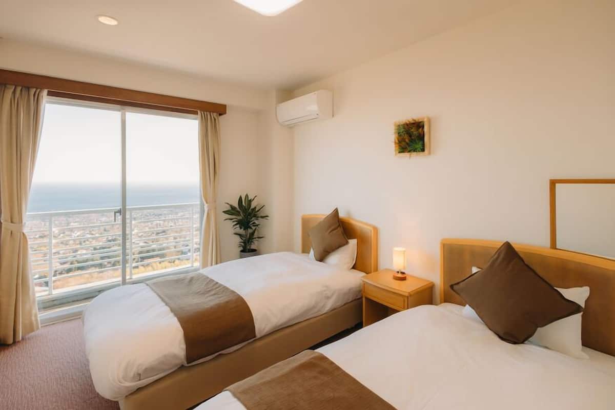 Une chambre d’hôtel avec deux lits, une grande fenêtre donnant sur la ville, un appareil de climatisation et une petite plante.