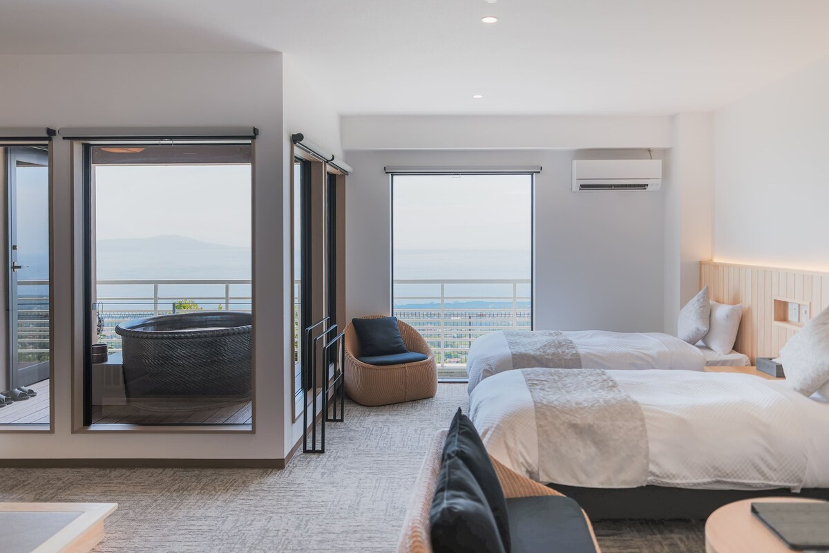 A hotel room with a balcony, a bed, a sofa, and a view of the cityscape.