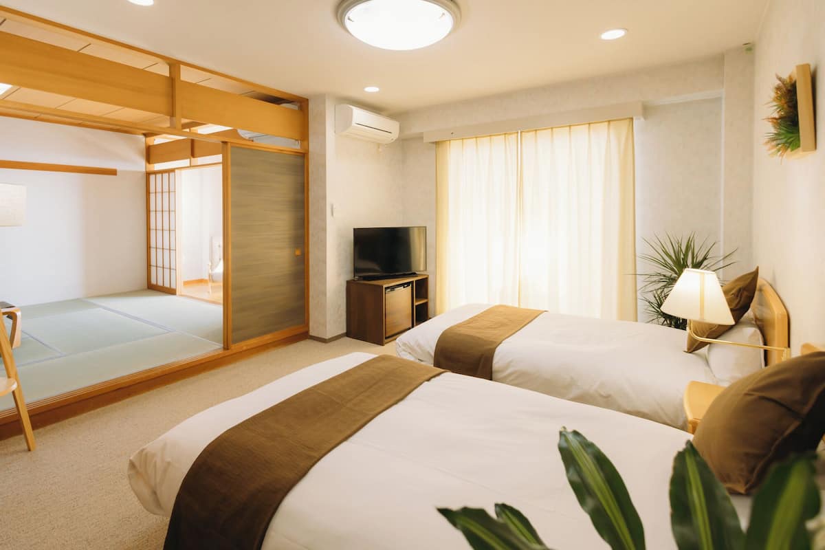 Une chambre d’hôtel avec un sol recouvert de tatamis, une télévision, un bureau et deux lits.