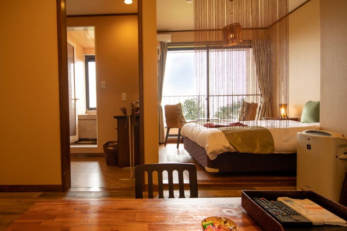 A hotel room with a bed, a desk with a computer, a chair, and a window with a view.