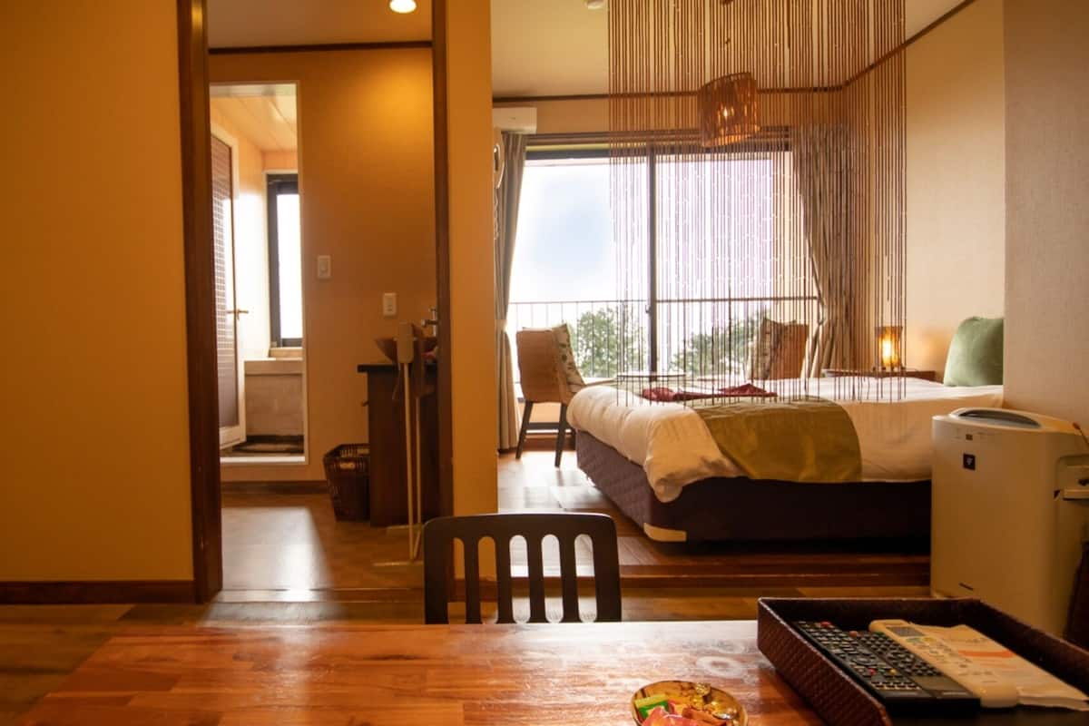 A hotel room with a bed, a desk with a computer, a chair, and a window with a view.