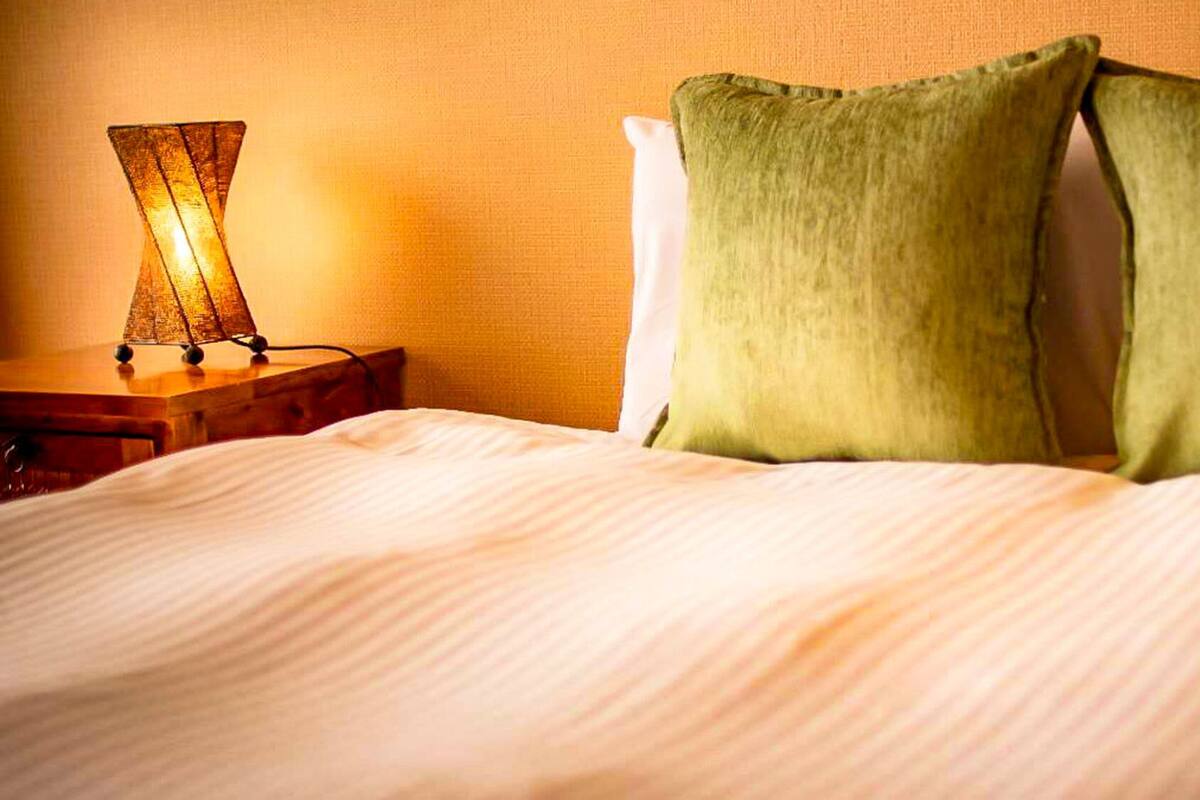 A neatly made bed with a white comforter and two green pillows, a bedside lamp, and a wooden nightstand.
