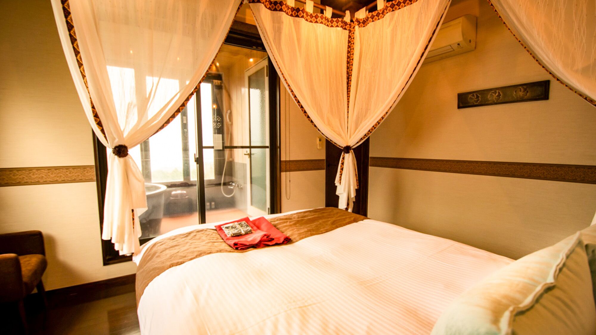 A hotel room with a bed, a chair, a window with curtains, and a sliding door leading to a balcony.