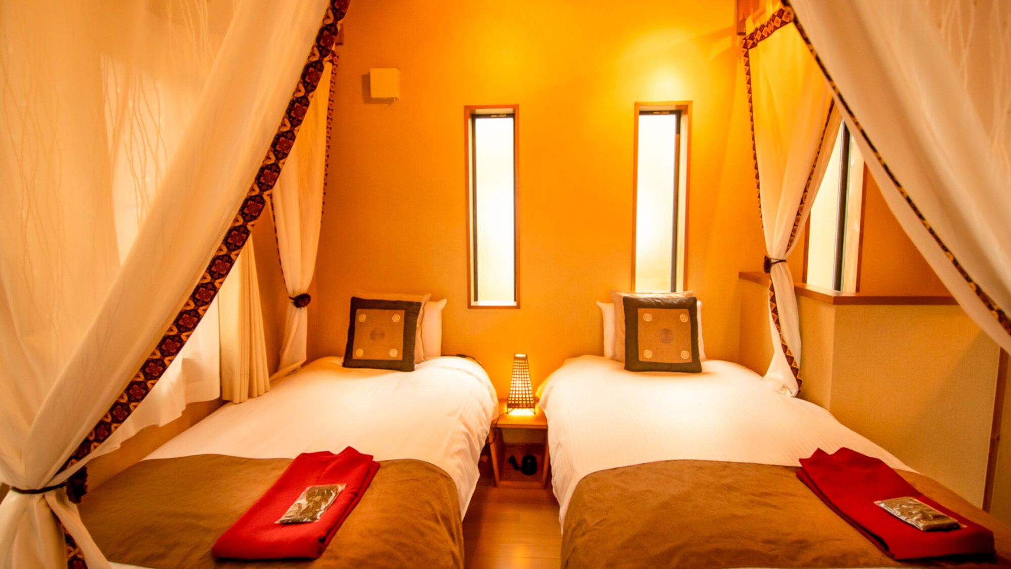 A room with two beds, each with a bedside table and a lamp, and a window in the center.