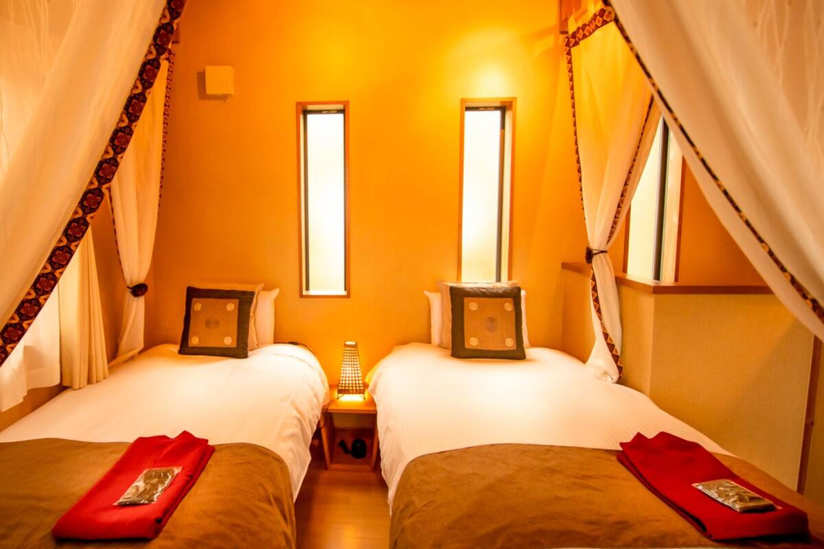 A room with two beds, each with a bedside table and a lamp, and a window in the center.