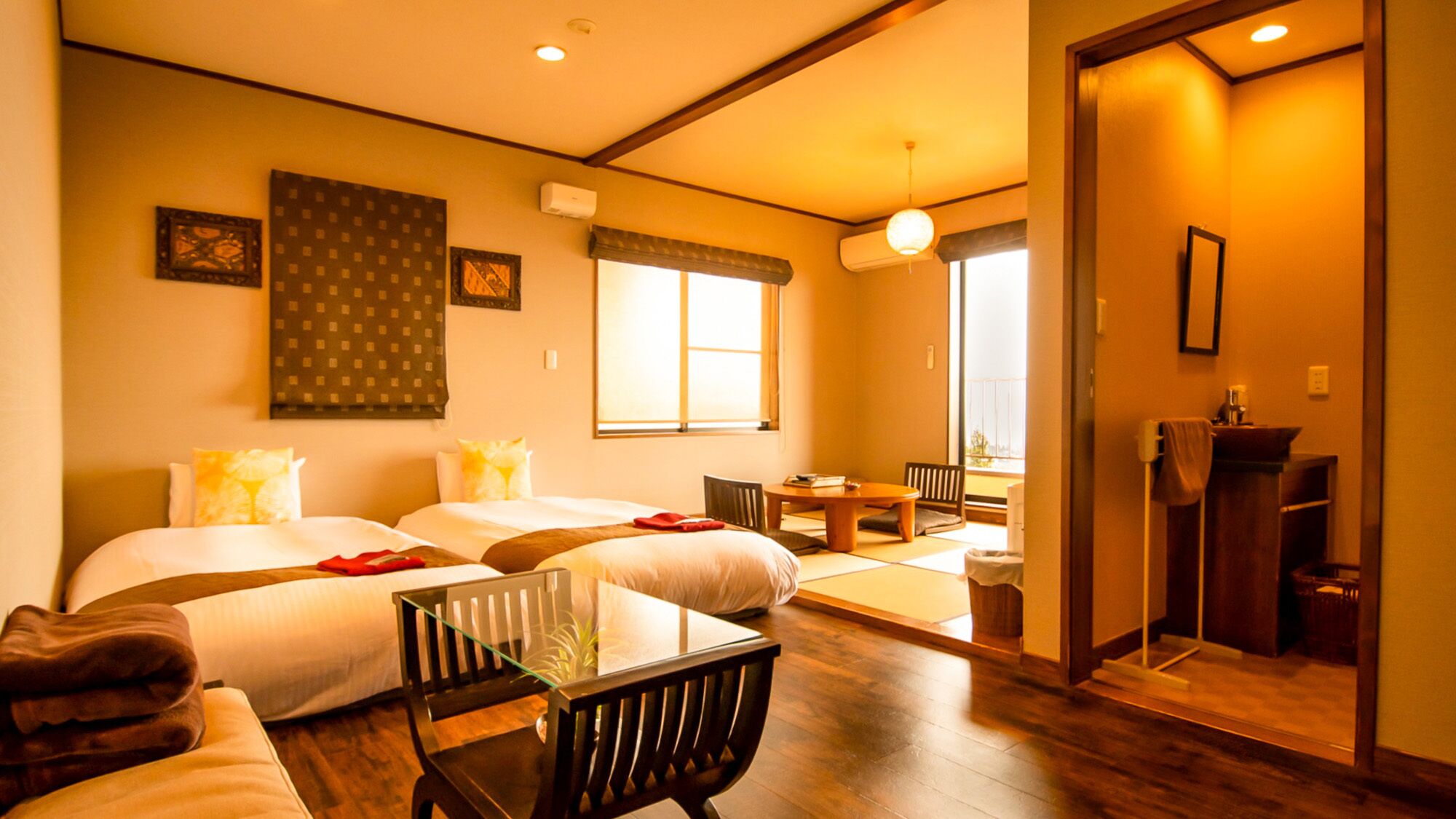 A hotel room with two beds, a dining table, a chair, a small table, and a mirror.