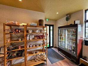 A room with a wooden shelf filled with various packaged goods, a refrigerator with beverages, and a door leading outside. - Sloth Glamping <tsushima> (Tsushima)