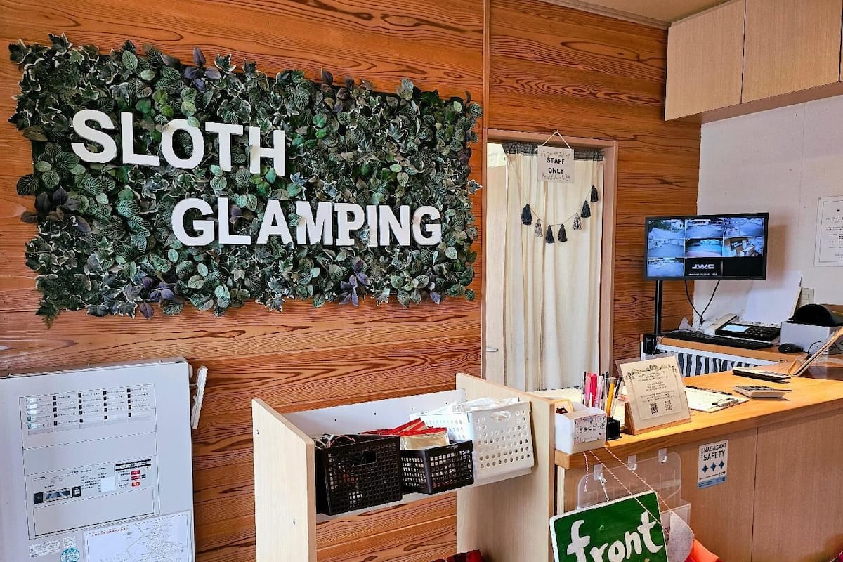 A room with a sign reading 'SLOTH GLAMPING,' a computer monitor, a desk with various items, and a map on the wall.
