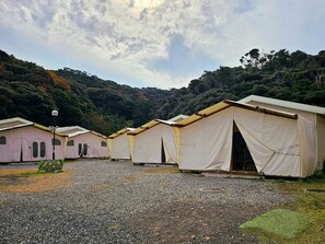 A row of simple, tent-like structures with a gravel ground, surrounded by dense forest. - Sloth Glamping <tsushima> (Tsushima)