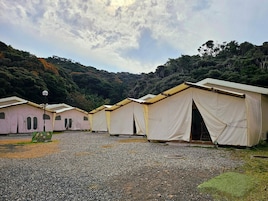 A row of simple, tent-like structures with a gravel ground, surrounded by dense forest.