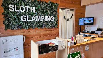A room with a sign reading 'SLOTH GLAMPING,' a computer monitor, a desk with various items, and a map on the wall.