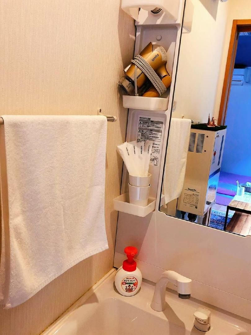 A bathroom with a white sink, a towel hanging on the wall, a mirror, and a shelf with toiletries.