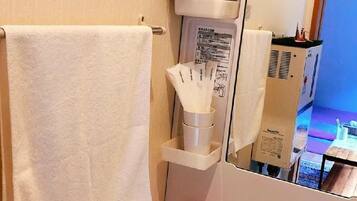 A bathroom with a white sink, a towel hanging on the wall, a mirror, and a shelf with toiletries.