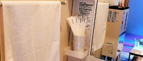 Un baño con lavamanos blanco, una toalla colgada en la pared, un espejo y un estante con artículos de aseo.
