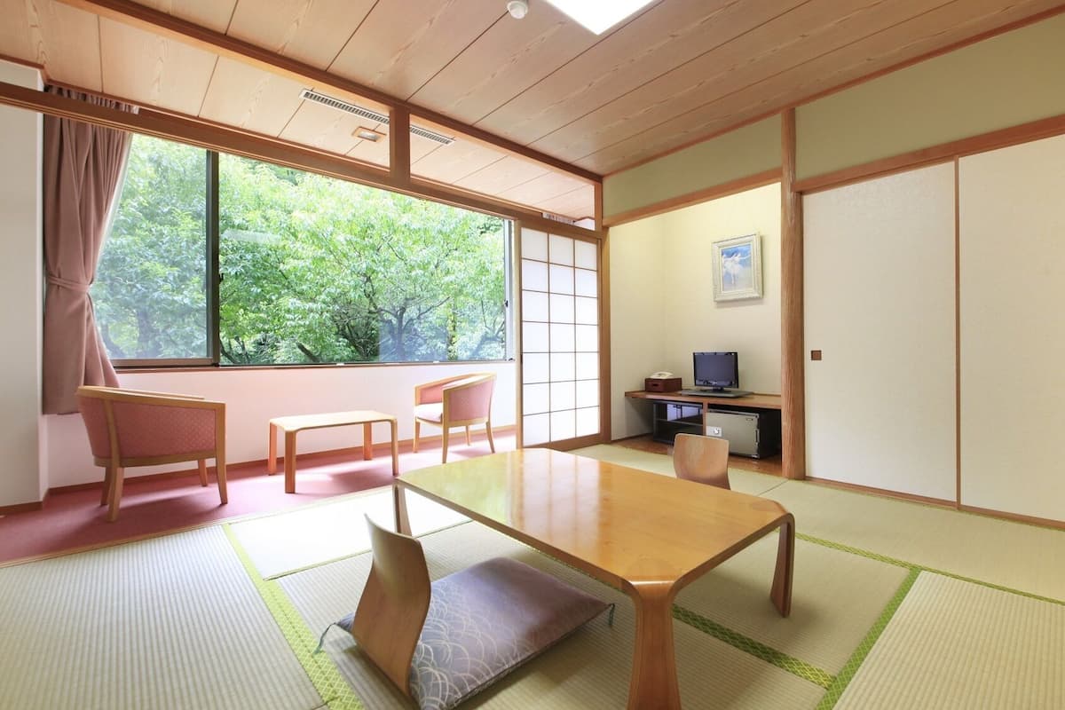 Una habitación japonesa tradicional con suelo de tatami, una mesa baja, un escritorio con computadora y puertas correderas.
