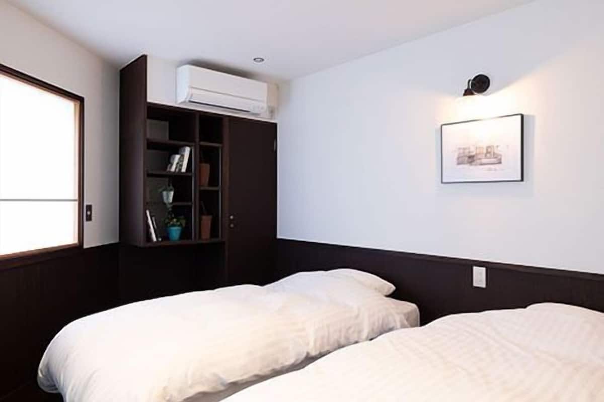 A bedroom with two beds, a wardrobe, an air conditioning unit, a wall-mounted light, and a framed picture.